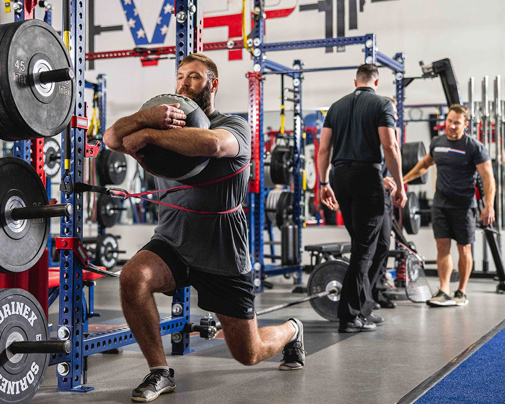 A man exercises with weights and a sandbag in a gym, associated with the Wounded Warrior Project.