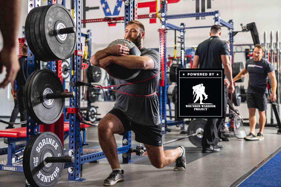 A man exercises with weights and a sandbag in a gym, associated with the Wounded Warrior Project.