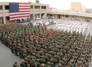 A military formation with soldiers in uniform and an American flag in the background, possibly a ceremonial event.